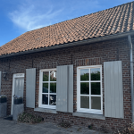 Bakstenen voorgevel van een woning met witte luiken; illustratie bij uitleg over het Carebrick systeem tegen optrekkend vocht.