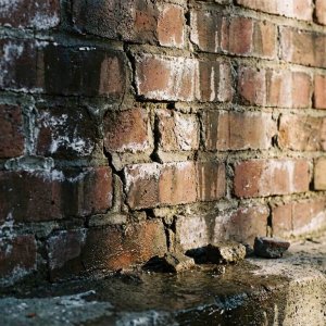 Beschadigde bakstenen muur met vochtschade, gebarsten voegen, witte zoutafzettingen en afgebrokkeld mortel