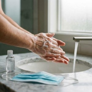 Handen wassen met antibacteriële zeep onder stromend water, handsanitizer en mondkapje op marmeren wastafel