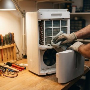 Technicus onderhoudt moderne luchtontvochtiger met zachte doek, interne filters zichtbaar, gereedschap op werkbank