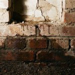 Doorsnede bakstenen muur met waterschade op twee niveaus: opstijgend vocht onderaan en infiltratie bovenaan