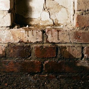 Doorsnede bakstenen muur met waterschade op twee niveaus: opstijgend vocht onderaan en infiltratie bovenaan