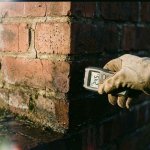 Vochtmeter meet waterschade op bakstenen muur met donkere vlekken en scheuren in voegen