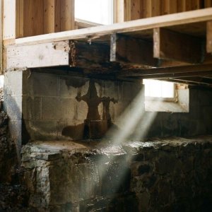 Doorsnede van huisfundering met vochtschade, donkere watervlekken op betonblokken en houten balken in kelder