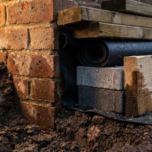 Doorsnede bakstenen muur met vochtproblemen en verschillende bouwmaterialen zoals behandeld hout en waterdichte membranen