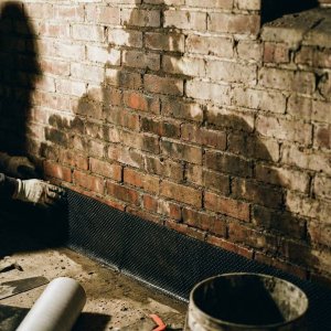 Professionele installatie van vochtbarrière in bakstenen fundering met zichtbare vochtschade en opstijgend vocht