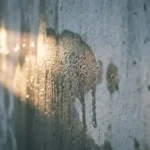 Waterdruppels stromen langs een koude betonnen binnenmuur met dramatische ochtendlichtval
