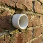 Witte keramische buis in verweerde bakstenen muur met waterdruppels, close-up met warme verlichting