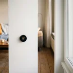 Slimme thermostaat toont lagere temperatuurinstelling op witte muur, droge ramen in warme Nederlandse woonkamer met houten vloer