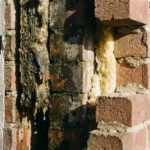 Doorsnede van een spouwmuur met doorweekte isolatie die druppelt van vocht, droge isolatie aan de andere kant