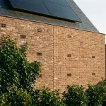 Nederlandse woning met keramische ventilatie-elementen in verweerde baksteen, groene klimop, zonnepaneel op dak
