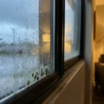 Waterdruppels condenseren op raamglas met schimmelvorming in hoekframe tijdens zware regenval