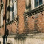 Historische bakstenen gevel met vochtplekken en keramische ventilatiebuizen in voegwerk, sierlijke boogvensters en kroonlijsten