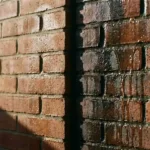 Doorsnede van bakstenen muur toont vochtproblemen: links lichte bevochtiging met waterdruppels, rechts zware watersaturatie met stromend water