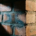 Bakstenen muur met donkere watervlekken in voegwerk en vochtdruppels op binnenoppervlak naast droog gedeelte