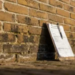 Nederlandse bakstenen muur met vochtschade en donkere vlekken vanaf de fundering, taxatieklembord tegen verweerde stenen