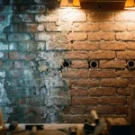 Doorsnede van bakstenen muur toont vochtschade met donkere vlekken links en gezonde droge bakstenen rechts, met keramische ventilatiepijpen