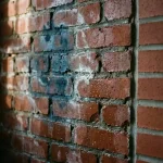 Verweerde bakstenen muur met vochtschade, donkere vlekken en uitbloeiingen naast droge bakstenen sectie