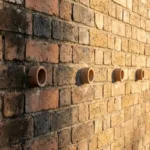 Verweerde bakstenen muur met keramische ventilatiebuizen toont vochtschade herstel van donkere natte vlekken naar droog metselwerk