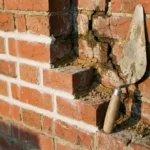 Rode bakstenen muur met nieuwe witte voegen naast verweerde, gebarsten mortel en professionele voegspaan
