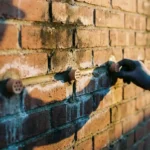 Vochtige bakstenen muur met keramische ventilatie-elementen in voegen, zonlicht benadrukt textuurcontrast