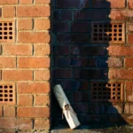 Verweerde bakstenen muur met CAREBRICK ventilatiesysteem, contrast tussen droge behandelde en vochtige onbehandelde sectie, garantiedocument