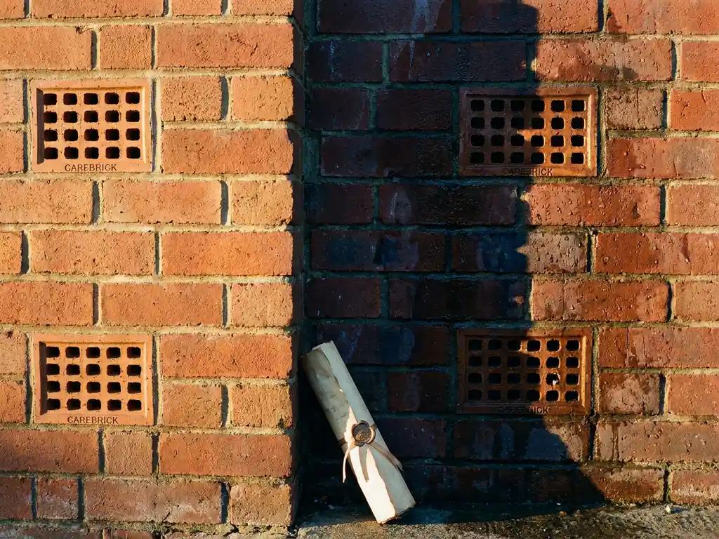 Verweerde bakstenen muur met CAREBRICK ventilatiesysteem, contrast tussen droge behandelde en vochtige onbehandelde sectie, garantiedocument