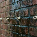 Vochtige bakstenen muur met witte ventilatiepijpjes in voegen, donkere vochtplekken en natuurlijk daglicht