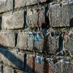 Berijpte bakstenen muur met waterdruppels en vochtschade in voegen, winterse condensatie en ijskristallen