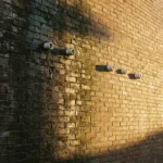 Verweerde bakstenen muur met donkere vochtplekken die overgaan naar droge stenen, witte keramische ventilatiebuizen geïnstalleerd