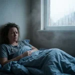 Persoon ligt onrustig in vochtige slaapkamer met condensatie op raam en schimmelplekken op muren
