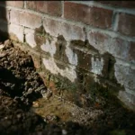 Doorsnede van bakstenen muurvoet met donkere watervlekken, vochtdruppels en staand water door slechte drainage