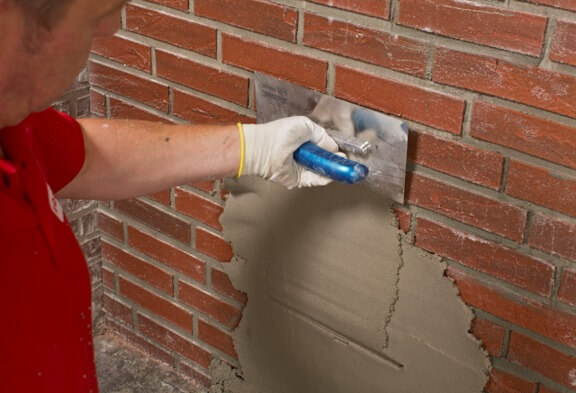 Een medewerker strijkt grijze pleister glad met een pleisterspaan.