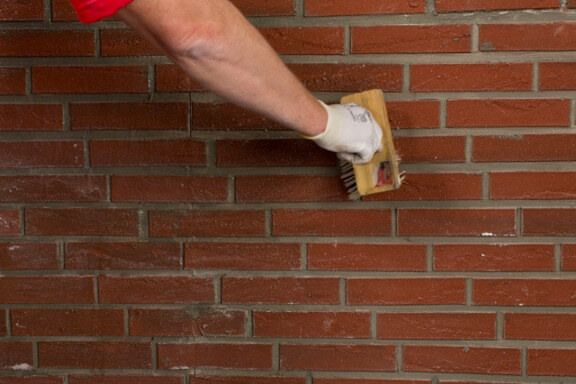 Een medewerker bewerkt een bakstenen muur met een borstel.